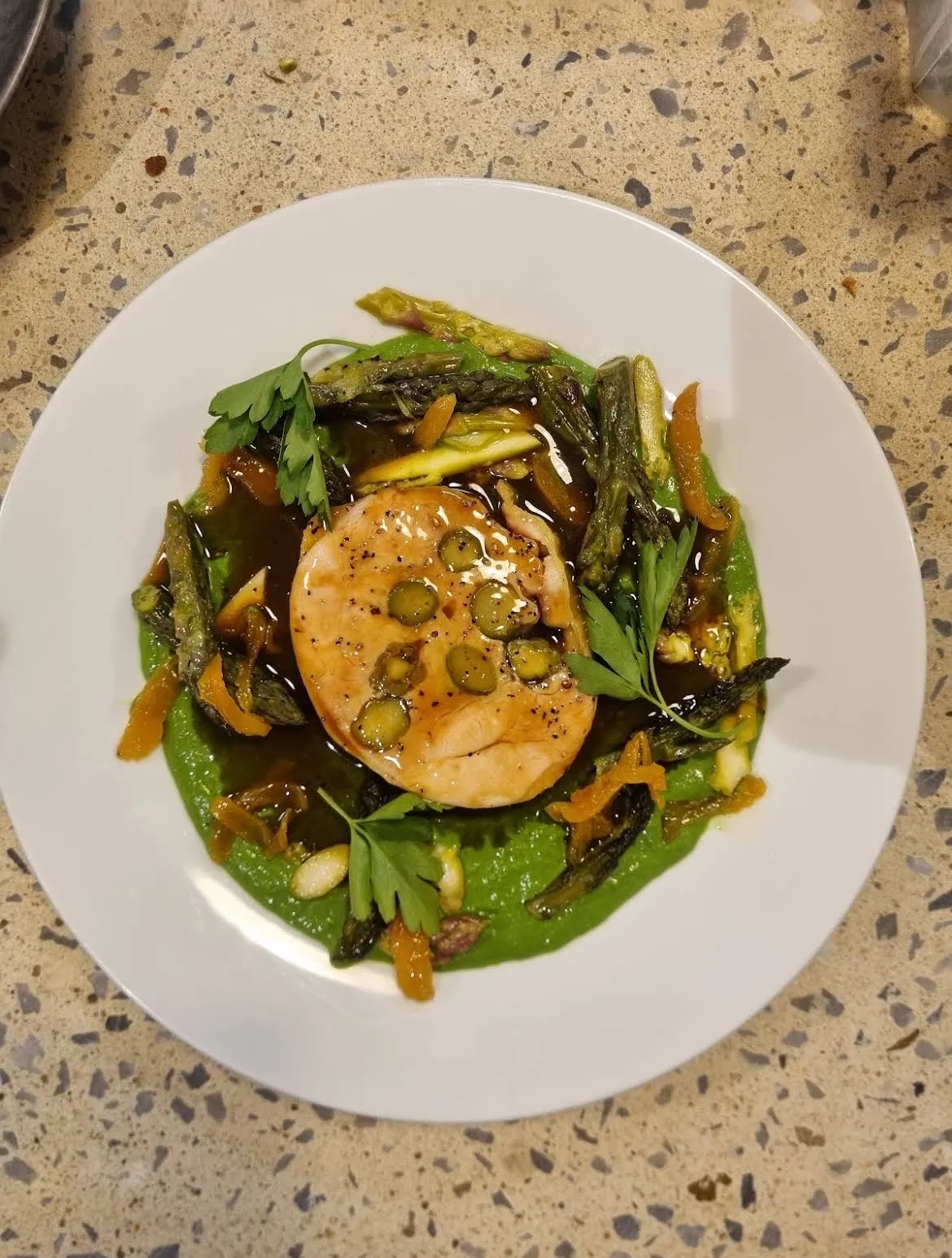 Une assiette de Mammouth, pain doré, sauce et légumes verts, sur le terrazzo