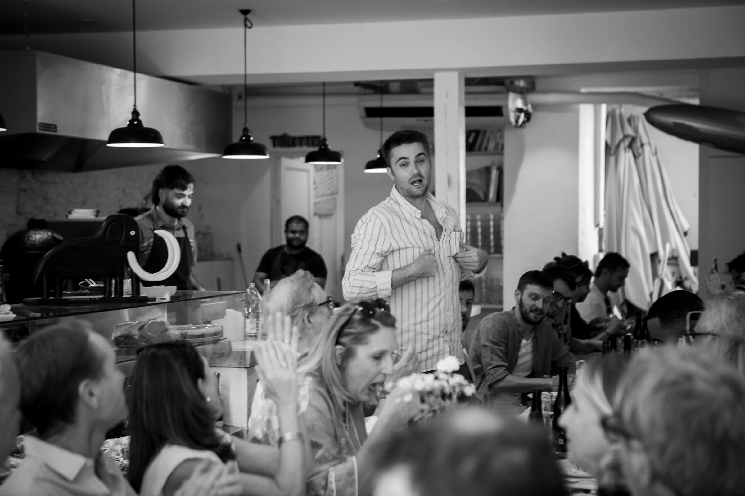 Un soir chez Mammouth : la grande tablée rit pendant qu’un convive debout fait le spectacle, l’équipe en cuisine derrière