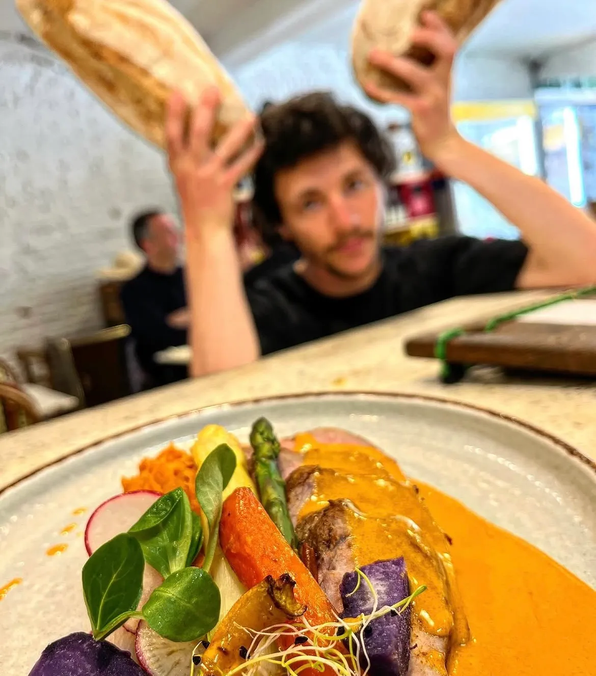 Au comptoir de Mammouth, un membre de l’équipe brandit deux miches de pain au-dessus d’une assiette de légumes rôtis, radis et viande en sauce