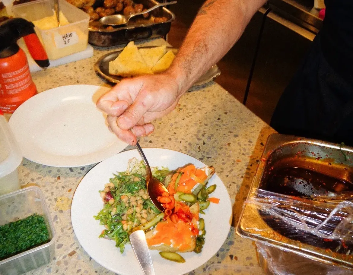 En cuisine chez Mammouth, une main nappe de sauce une assiette de pois chiches, roquette et tartine de poisson fumé